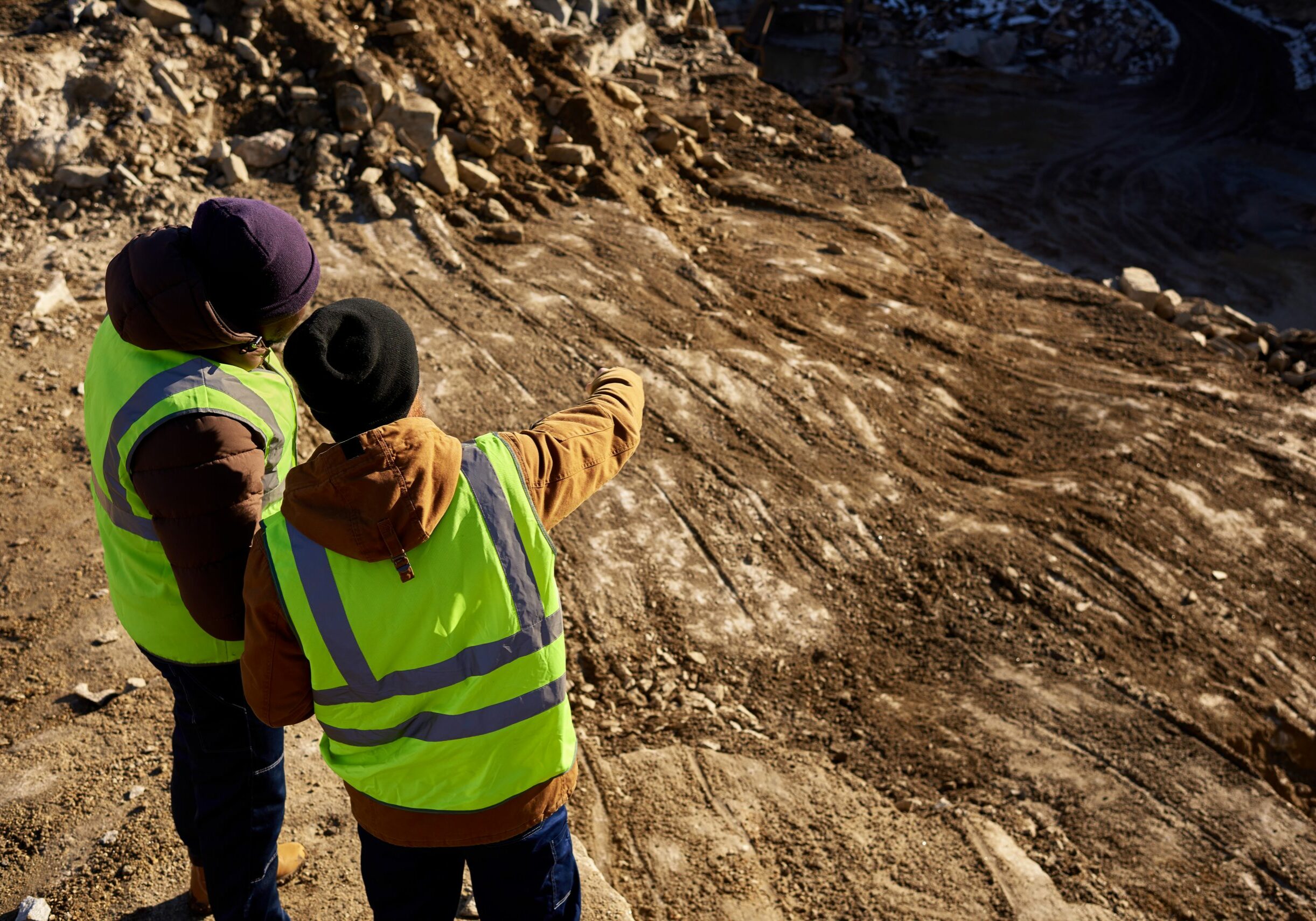 Miners in Quarry Back view portrait of two industrial workers wearing reflective jackets, one of them African, standing on cliff overlooking mineral mines on worksite, copy space